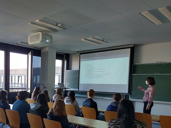 Gezeigt wird ein Foto von in einem Seminarraum sitzenden Besuchern, die einem Vortrag folgen.