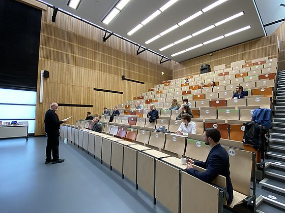 WEH-Kolloquium 2024 an der HHU Düsseldorf. Bild: Isabella Kappner Jurymitglieder und Gäste sitzen in einem Hörsaal. Vorne spricht ein Dozent.
